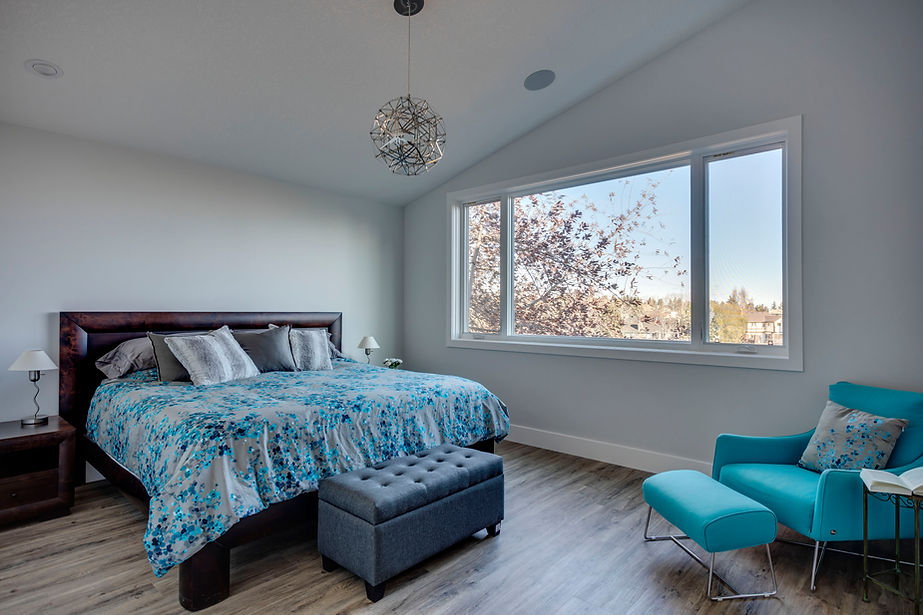 A light and bright bedroom with an angled roof and a hanging light over a double bed. A large window with views of trees outside on the right hand side.